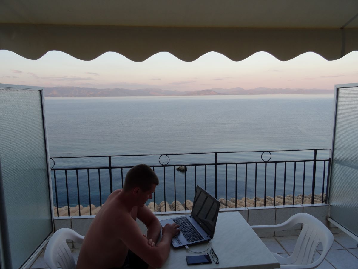 man working on laptop on a balcony in corfu greece